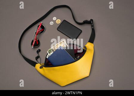 yellow belt bag for women and men on a dark gray background with accessories: for travel. copy space. top view. trend colour 2021, Pantone. Stock Photo
