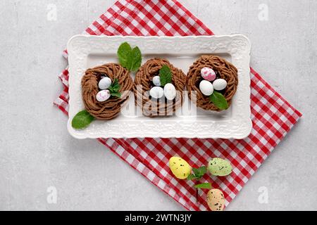Easter chocolate cookies in the shape of Nests with sweet eggs on white plate on red napkin with mint leaves. top view Stock Photo