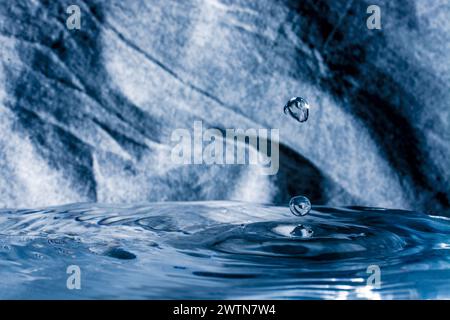 Photograph of water droplet hitting water surface and bouncing back up frozen in the air by flash. Stock Photo