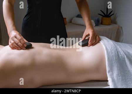 Woman enjoying hot stone massage on joints, muscles, and fingers at spa Stock Photo