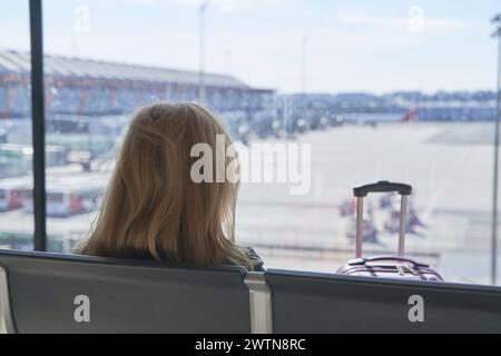 silhouette of an unrecognizable middle-aged woman sitting looking out of the glass of an airport terminal Stock Photo