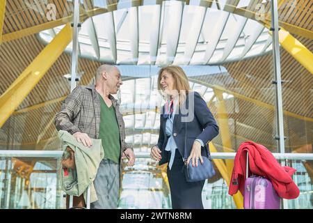 middle-aged adult traveler couple talking at bus terminal or airport waiting to go on a trip or honeymoon Stock Photo