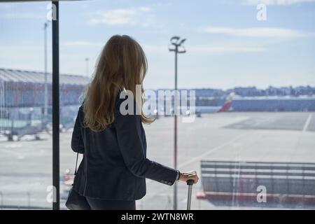 unrecognizable silhouette of woman looking out of window in airport terminal at airplanes Stock Photo