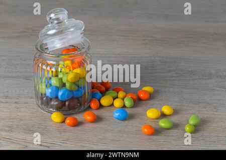 Peanuts in multi-colored icing in a glass jar on a wooden table Stock Photo