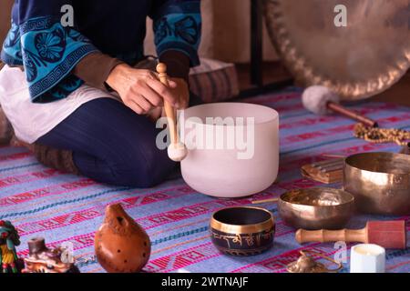 Close-up of a woman's hands playing a quartz singing bowl, while guiding a sound meditation surrounded by other instruments such as Tibetan singing bo Stock Photo