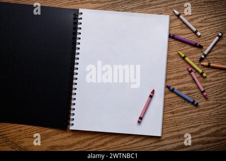A top view of assorted crayons and a blank notebook on a wooden table Stock Photo
