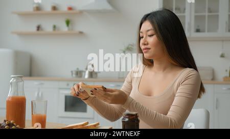 Asian housewife chinese korean japanese girl put on bread chocolate paste apply sweet jam on toast multiethnic woman cook breakfast at home cooking Stock Photo
