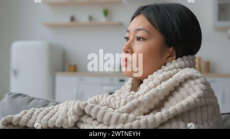 Depressed upset lonely Asian woman look in side think suffer apathy sadness depression alone chinese japanese girl cover in blanket in home kitchen Stock Photo