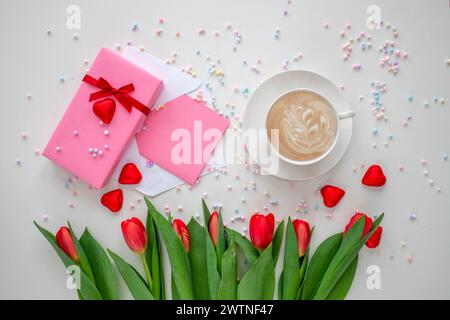 Mother's Day decorations concept. Top view photo of trendy gift boxes with ribbon bows, spring tulips cup of coffee and greeting card with copy space. Stock Photo