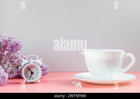 Alarm clock, lilac flowers and cup of coffee on light background. Spring and early morning concept. Stock Photo