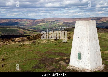 Man leaning resting against the Trig point on Eyam Moor off William Hill road while walking and back packing in the Derbyshire Peak District Stock Photo