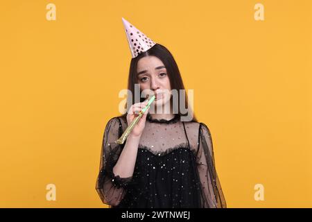 Woman in party hat with blower on orange background Stock Photo