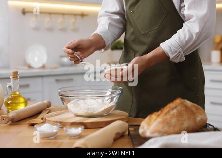 Making bread. Man putting dry yeast into bowl with flour at wooden table in kitchen, closeup Stock Photo