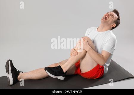 Man suffering from leg pain on mat against grey background Stock Photo