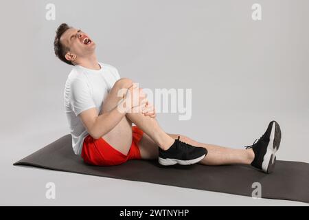Man suffering from leg pain on mat against grey background Stock Photo