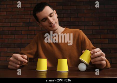Shell game. Man showing ball under cup at wooden table, low angle view Stock Photo