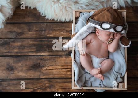 Cute newborn baby in aviator hat sleeping on wooden background, top view. Space for text Stock Photo