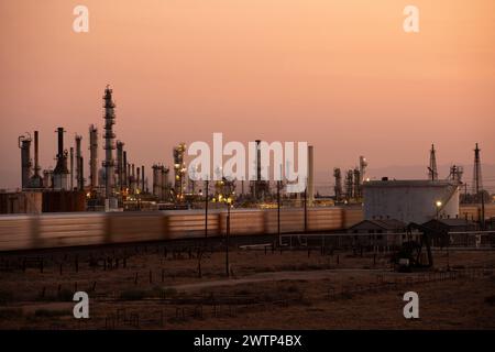 A train passes by an oil refinery at sunset in Bakersfield, California, USA. Stock Photo