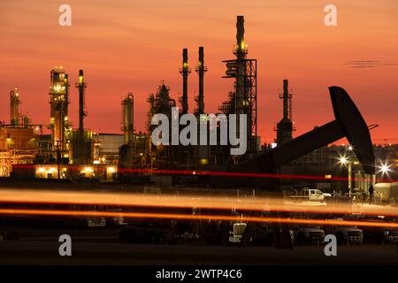 Evening traffic passes by an oil pump jack and refinery in Bakersfield, California, USA at sunset. Stock Photo