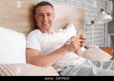 Middle-aged man in bed checking pills description at home Stock Photo