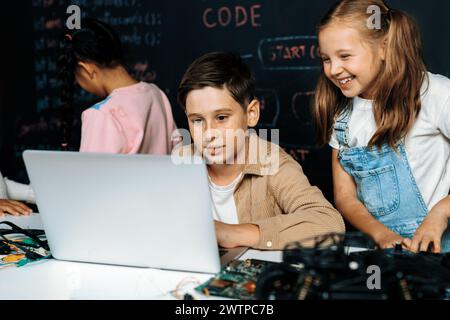 In classroom student in STEM class learning about coding robotics car. Brown shirt Schoolboy and white bib schoolgirl watching laptop and discussing Stock Photo