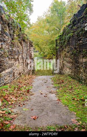 A gray path runs between two high mossy stone walls, with red autumn leaves on the grass, at Harpers Ferry National Historical Park. Stock Photo