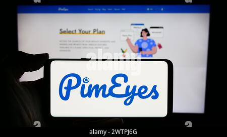 Person holding cellphone with logo of facial recognition search company PimEyes in front of business webpage. Focus on phone display. Stock Photo