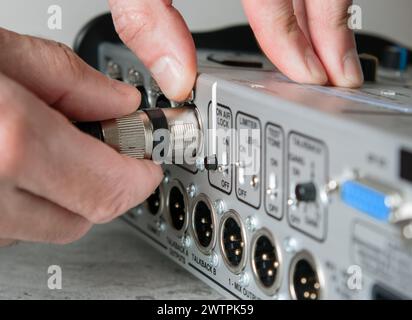 A male hand unplugs a male XLR cable from the input of a mixing console. Stock Photo