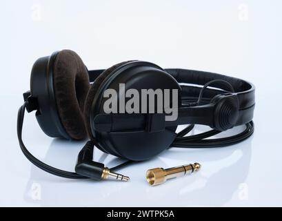 Professional DJ black headphones with velor ear pads and gold-plated 6.3mm jack adapter on a white background with reflection Stock Photo