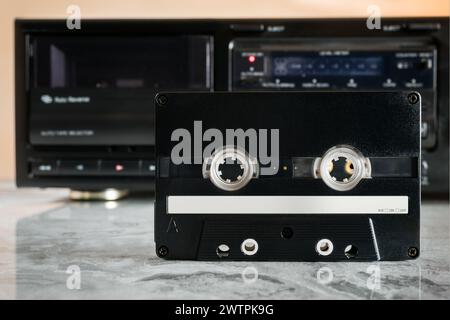 Black audio cassette with empty white space for notes in front of cassette deck on polished marble shelf with reflection Stock Photo