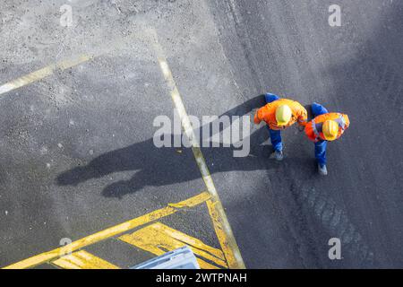 Two construction workers in hard hats walk over tarmac. They cast long shadows. Stuttgart, Baden-Wuerttemberg, Germany Stock Photo