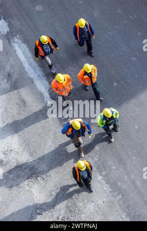 Several construction workers wearing hard hats walk over tarmac. They cast long shadows. Stuttgart, Baden-Wuerttemberg, Germany Stock Photo