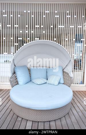 Round comfortable sofa with blue bed linen. Sofa with cushion in the outdoor garden. Aesthetic room divider on the back side. Stock Photo