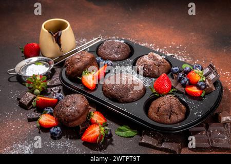 Chocolate muffins with berry. Baking muffin pan with homemade sweet dark chocolate cupcakes with cocoa sauce, sugar powder and fresh strawberry, blueb Stock Photo