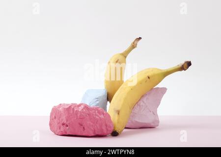 a scenographic composition of a still life composed of ripe bananas and brightly painted pebbles against a pink and white background. Vivid colors and Stock Photo