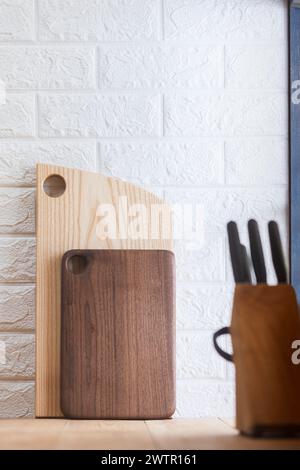 Wooden cutting boards leaned against the wall. In the foreground is a set of kitchen knives. Stock Photo