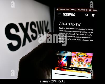 Person holding cellphone with webpage of annual film and media event South by Southwest (SXSW) in front of logo. Focus on center of phone display. Stock Photo