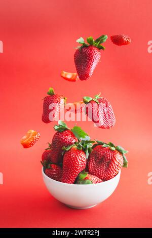Strawberries falling on a white bowl. Vibrant red background. Stock Photo