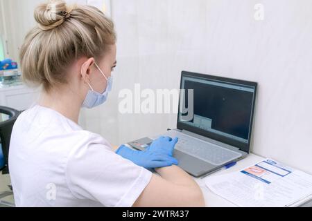 Dentist assistant or nurse working on laptop in dental office wearing medical gloves and mask Stock Photo