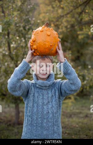 Boy in a knitted blue sweater is holding in his hands ugly orange pumpkins. Deformed orange pumpkins with a damaged, ugly skin. Thanksgiving, harvest, halloween concept.  Stock Photo