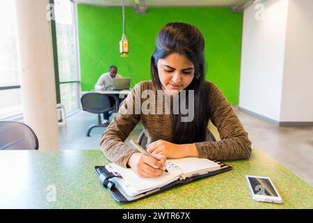 Young student making notes Aachen, Germany. Young, female Indian university exchange student working on a dormatory work desk, using her smartphone and analog notebook. MRYES Aachen Universiteit vsan Aachen Nortrhein-Westfalen Duitsland Copyright: xGuidoxKoppesx Stock Photo