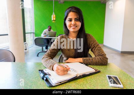 Young student making notes Aachen, Germany. Young, female Indian university exchange student working on a dormatory work desk, using her smartphone and analog notebook. MRYES Aachen Universiteit vsan Aachen Nortrhein-Westfalen Duitsland Copyright: xGuidoxKoppesx Stock Photo