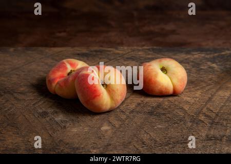Three ripe chinese flat peach fruits or saturn peaches on vintage wooden background. Stock Photo