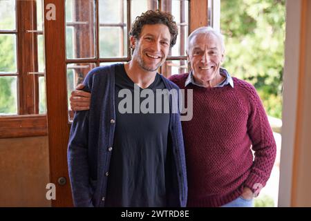 Son, senior father and portrait in home by front door with hug, smile and bonding with connection. Men, elderly dad and adult child with embrace for Stock Photo