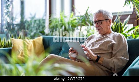 Senior man using digital tablet while sitting on sofa in living room at home Stock Photo
