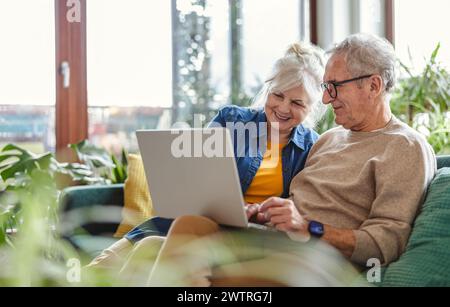 Senior couple using laptop while sitting on sofa in living room at home Stock Photo