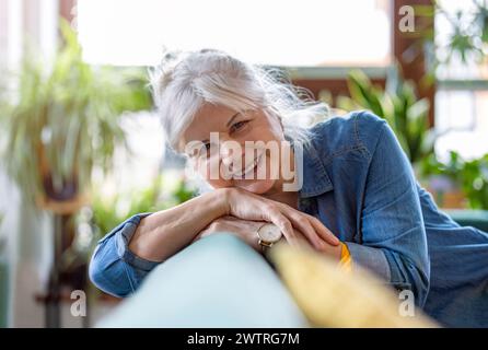 Portrait of smiling senior woman sitting on sofa in living room at home Stock Photo
