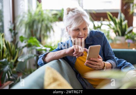 Smiling senior woman using smart phone while sitting on sofa at home Stock Photo