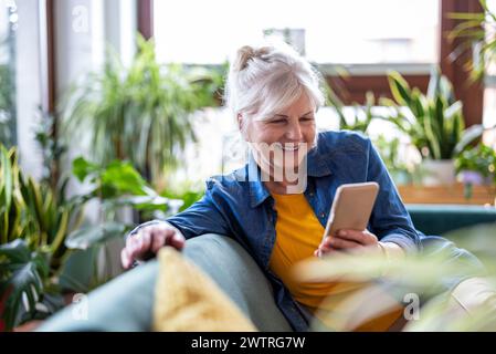 Smiling senior woman using smart phone while sitting on sofa at home Stock Photo