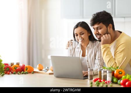 Happy loving young indian spouses using laptop while cooking Stock Photo